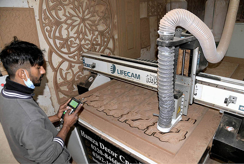 A carpenter carving a beautiful design on a wooden sheet by machine at his workplace in the city.