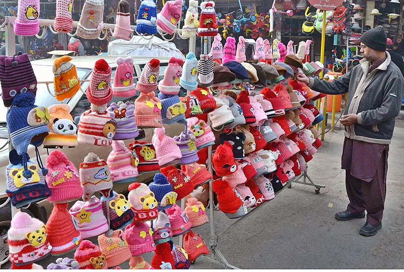 A vendor arranging and displaying the colorful winter caps to the customers on the roadside setup at a local market