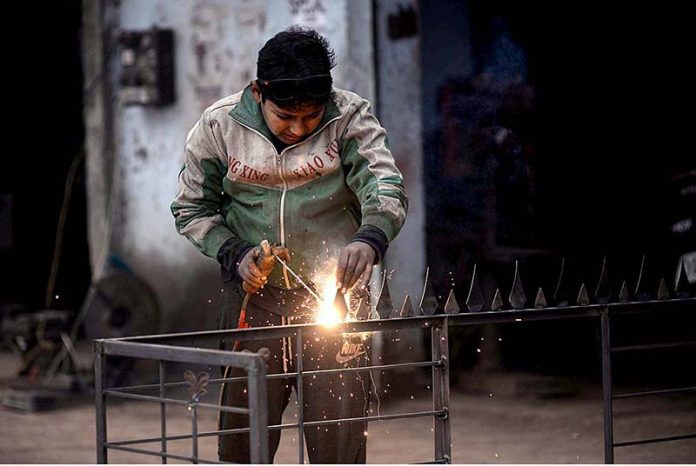 A youngster labourer busy in welding the iron grill at his workplace