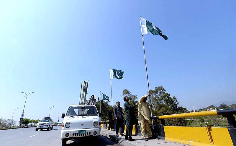 CDA workers fixing national flags on flyover at Srinagar Highway in connection with National Day of Pakistan