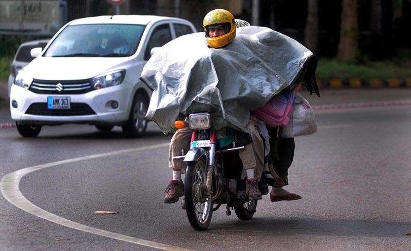 A family on his way to cover with sheet to protect from rain on motorbike at Federal Capital