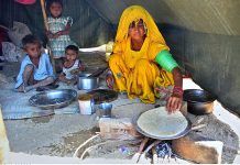 A gypsy woman preparing bread (Roti) for children in her makeshift house at Latifabad