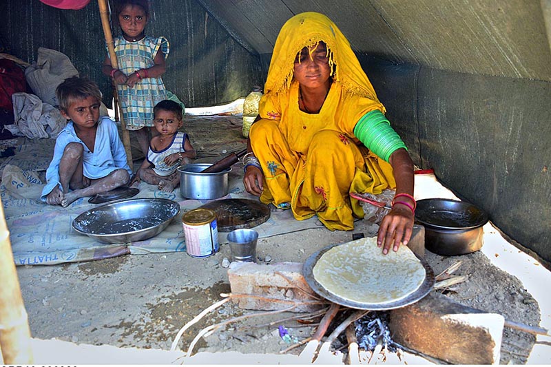 A gypsy woman preparing bread (Roti) for children in her makeshift house at Latifabad