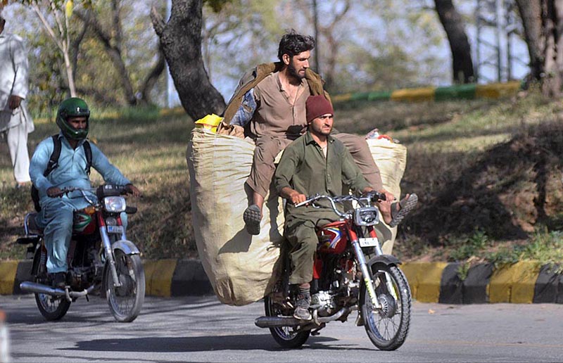 Scrap collector sitting on sheaf recycle items while riding on motorbike after collection from garbage dumps to sell and earn their livelihood