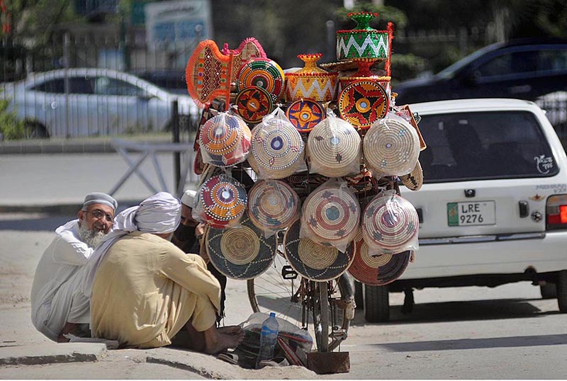 A hawker is selling beautiful and colorful handicrafts on his cycle on a roadside in Federal Capital
