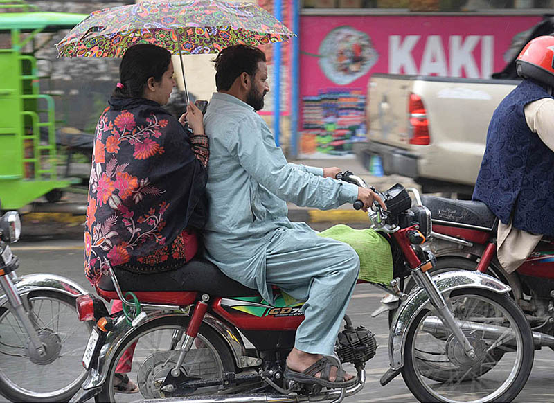 A woman holding an umbrella to protect from rain while riding on motorcycle in the Provincial Capital