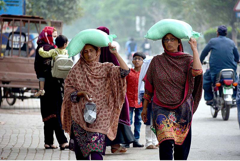 Women are returning back after getting free flour bags from a distribution center under Prime Minister’s Ramzan Relief Package for deserving families