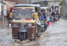 Commuters passing through rain water accumulated on the road during heavy rain in the city