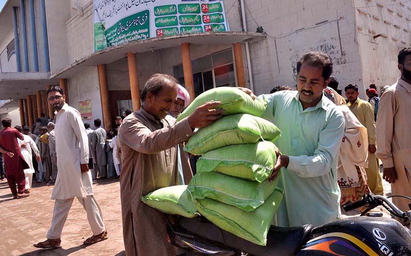 People receive free flour bags from a distribution point under Prime Minister’s Ramazan package for deserving families at Sattelite Town