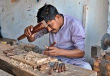 A worker busy in carving design on the wooden piece at his workplace
