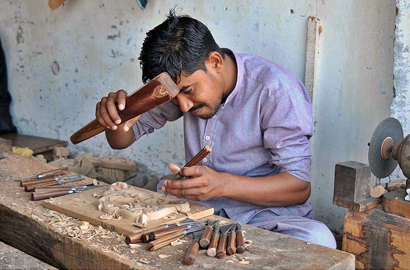 A worker busy in carving design on the wooden piece at his workplace