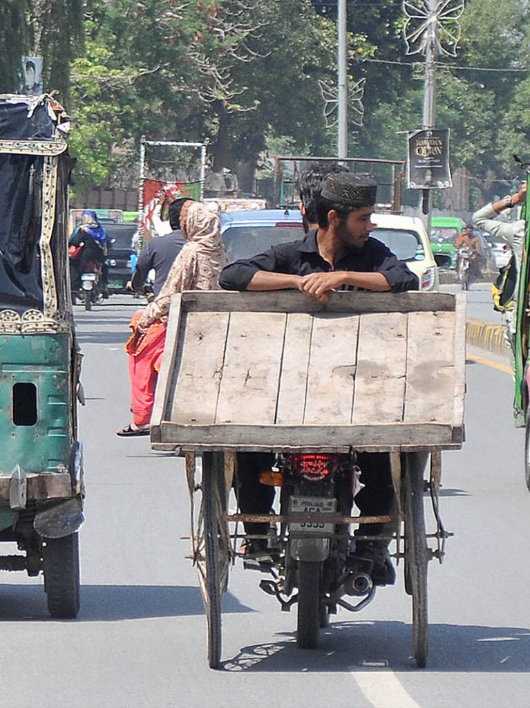 <em>A person holding a hand cart while sitting on the rear seat of a motorcycle</em>