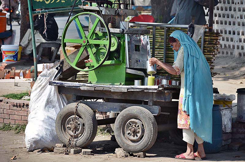 An old woman is making and selling sugarcane juice on a roadside setup in connection with International Women's Day