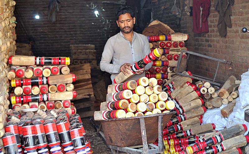 Labourer loading colorful part of traditional bed (Charpai) on hand cart to deliver in market at his workplace