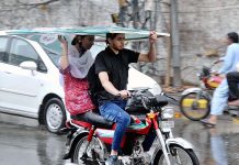 A woman holding a Banner Flex to protect from rain while riding on motorcycle in the Provincial Capital