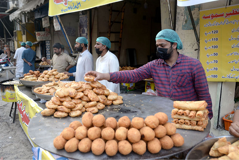 A shopkeeper is attracting customers by displaying samosas, kachoris, and chicken rolls at his workplace