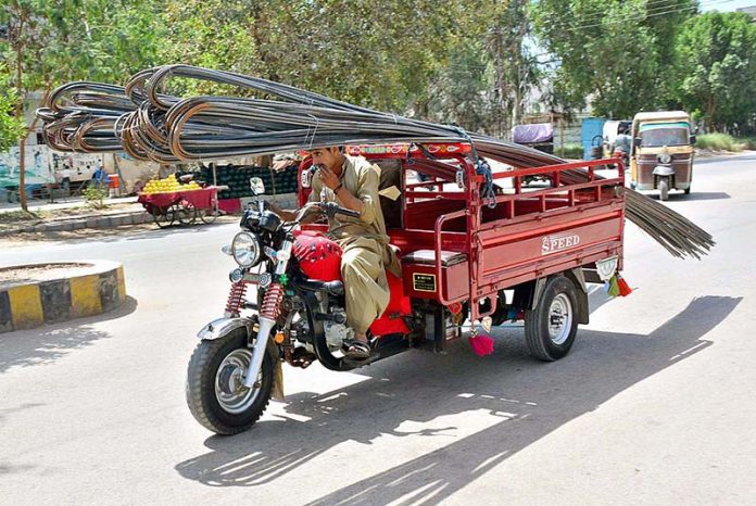 A tri-cycle rickshaw holder on the way loaded with iron rods at Latifabad.