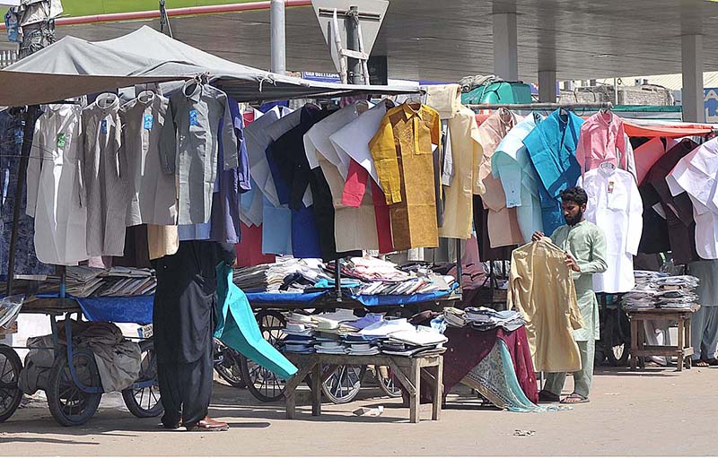 A vendor is arranging and displaying old clothes to attract customers at his roadside setup.