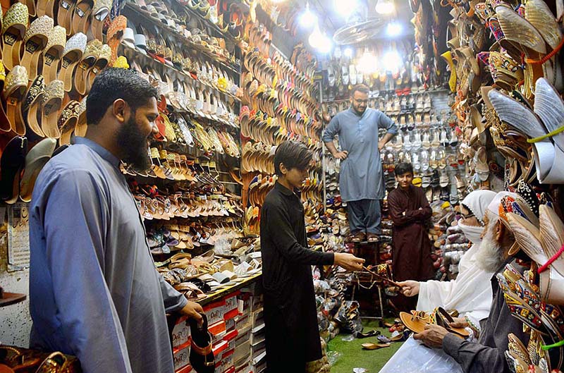 Customers selecting and purchasing shoes from a shopkeeper during preparation of upcoming Eid-Ul-Fitr at Sadar Bazar.