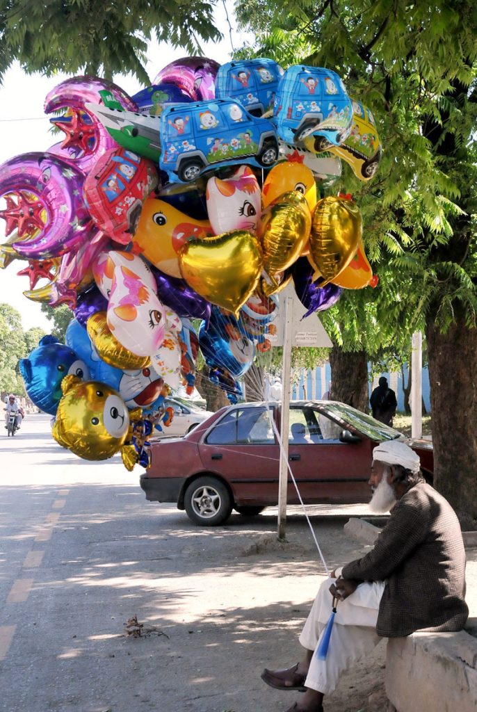 An old man selling colorful balloons to Attract costumers at Roadside.