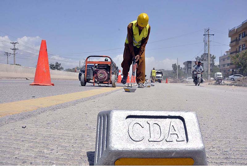A laborer is busy in installing cat eye on carpeted IJP road in the Federal Capital