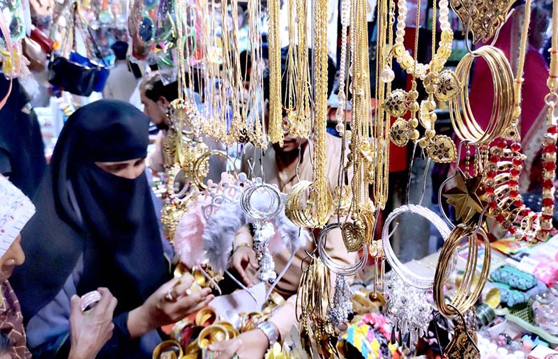 A woman selecting and purchasing artificial jewelry at a stall in Resham Gali in preparation of Eid-ul-Fitr festival