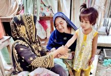 A vendor wearing bangles to a girl at Resham Gali in preparation of Eid-ul-Fitr festival