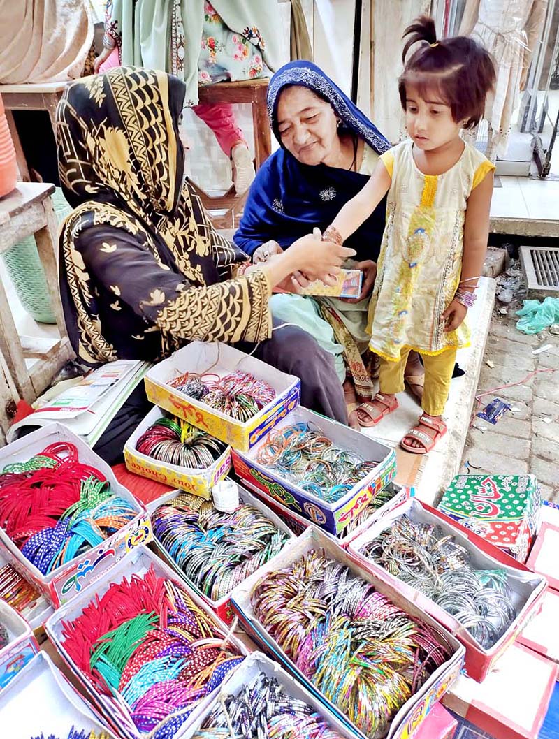 A vendor wearing bangles to a girl at Resham Gali in preparation of Eid-ul-Fitr festival