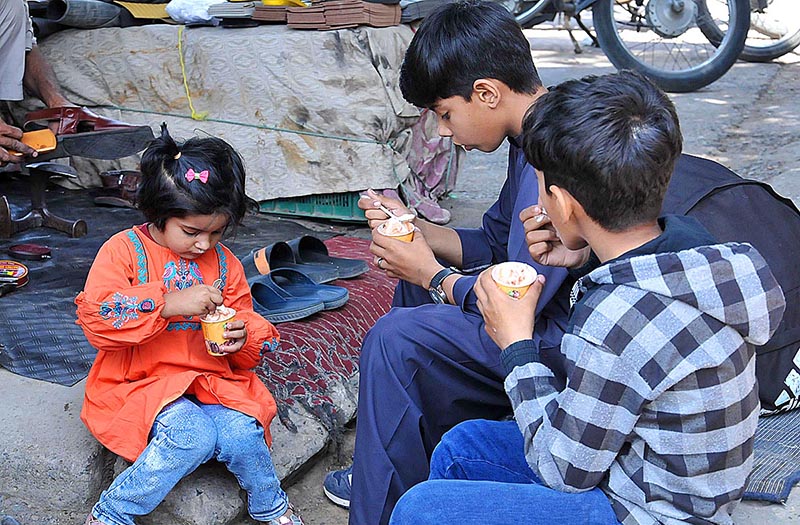 Children eating ice cream while sitting on the roadside at G9 Markaz