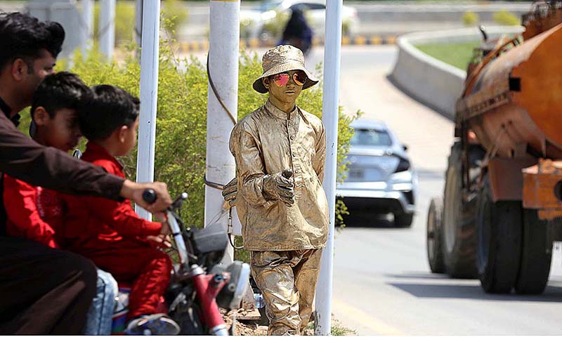 Golden man is standing on a roadside to earn some livelihood in the Federal Capital