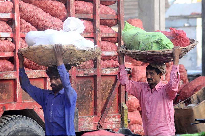 Daily wages laborers carrying baskets loaded with vegetables on their heads at a vegetable market