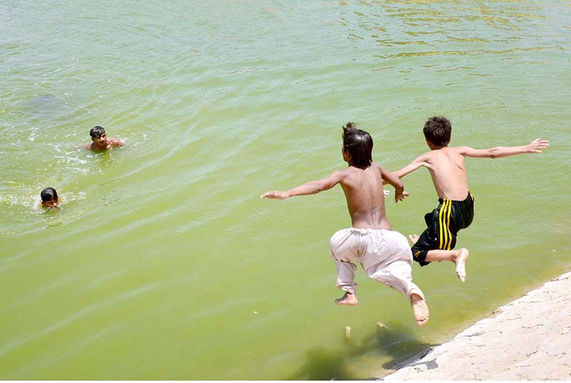 Youngsters jumping into a water pond for bathing to get some relief from hot weather in the city