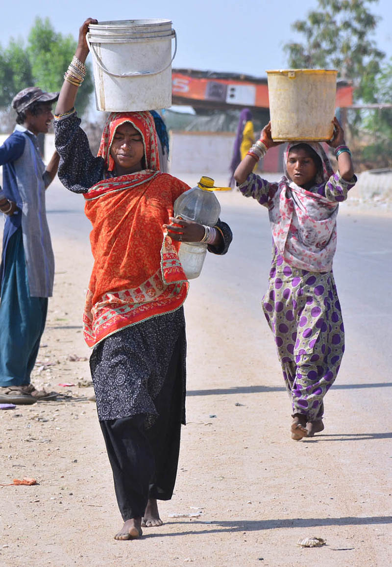 Gypsy women carrying pots on her head back after filling clean water at Latifabad