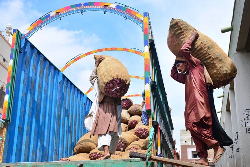 Workers loading onion sacks on a delivery truck at vegetable market