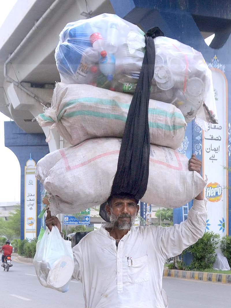 An elderly person on the way carrying plastic sacks on his head