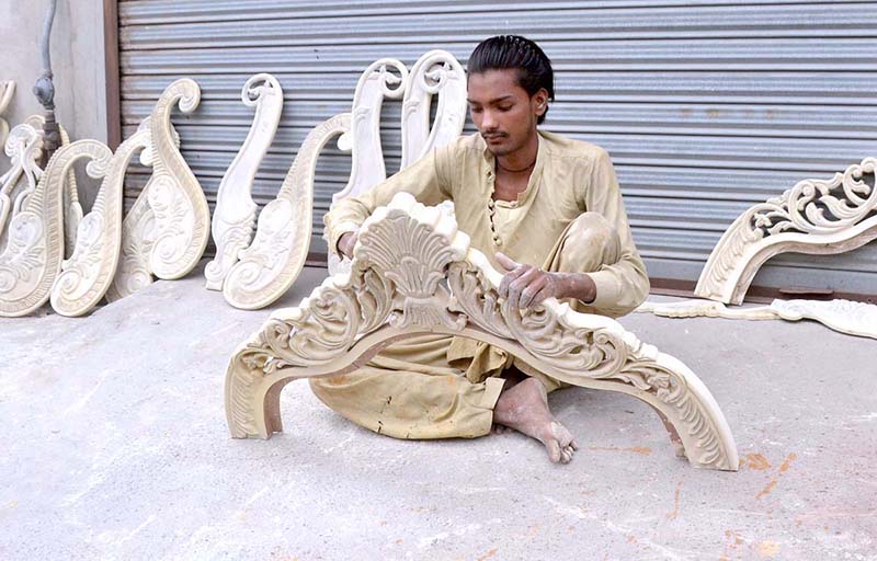 A carpenter is painting a wooden piece that will be used for furniture
