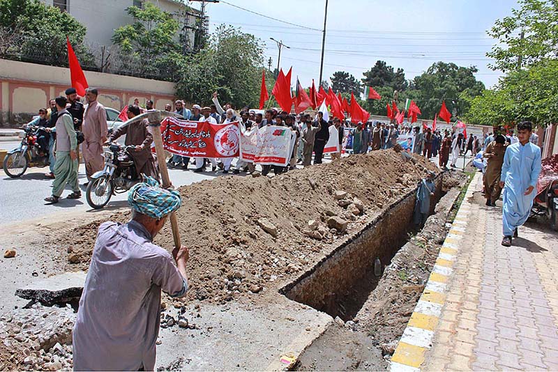 While a rally advocating for the rights of labourers passes by, laborers are hard at work digging a road to install a gas pipeline behind the CM Secretariat, holding pro-labor banners as they work