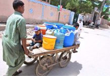 A person pushing hand cart loaded with water canes after filling clean water from filter at Latifabad