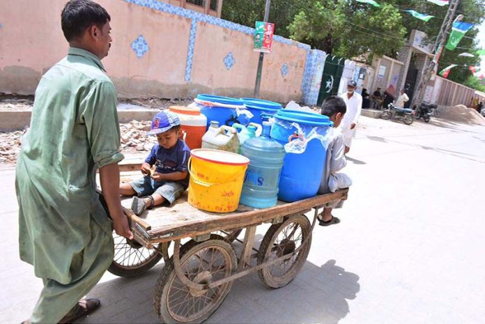 A person pushing hand cart loaded with water canes after filling clean water from filter at Latifabad