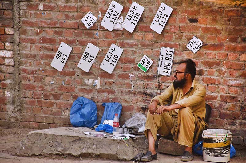Vehicle number plate maker waits for the customers at his road side setup in the city