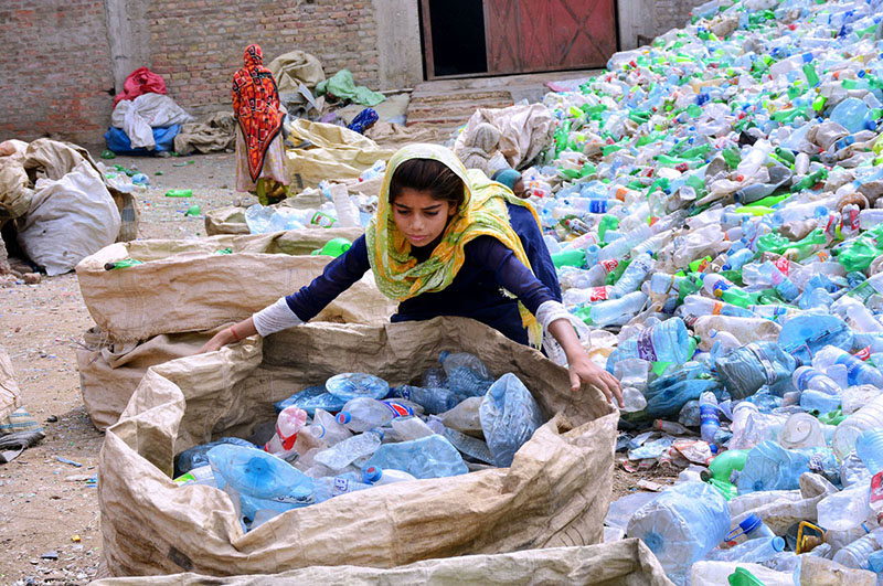 A labourer girl busy in filling their bag with used plastic bottles at local factory