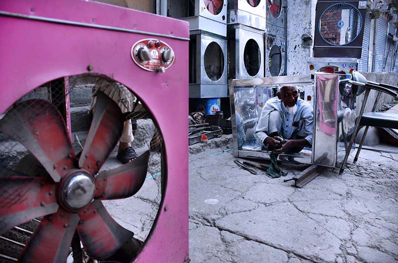 A worker makes frame box for room cooler using sheets of iron at his work shop