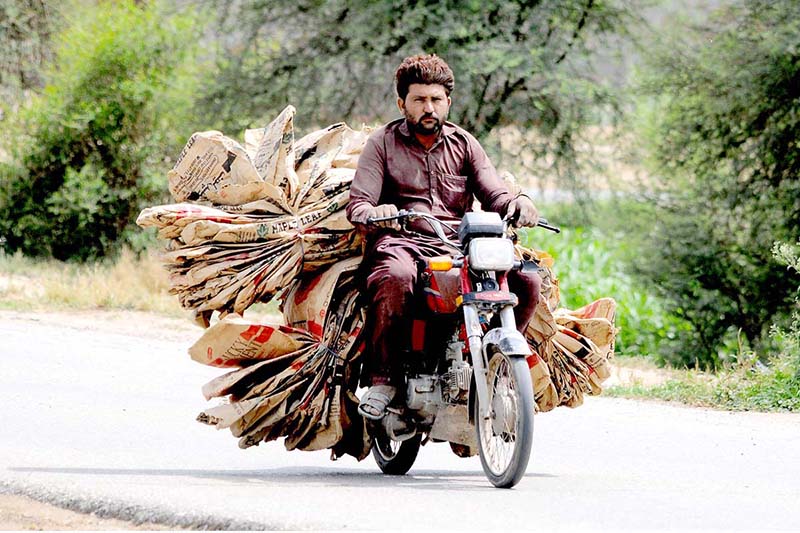A person is riding his motorcycle on the way, carrying a load of empty cement bags collected from different points in the city