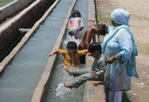 Children bathing in running tub well to get relief from scorching hot weather