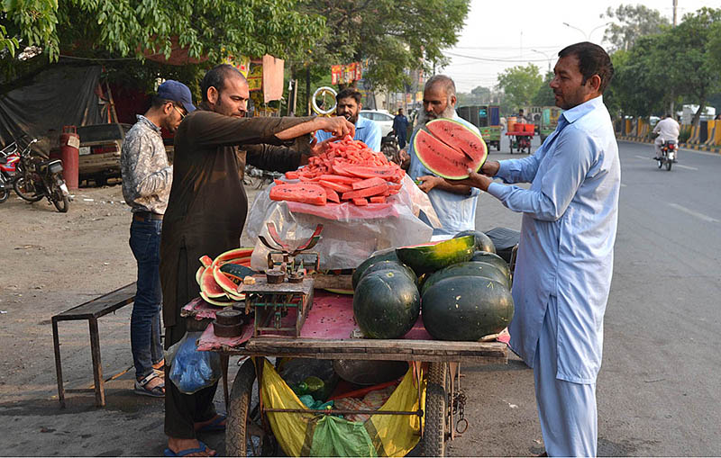 Customers are buying and eating watermelons from a roadside vendor
