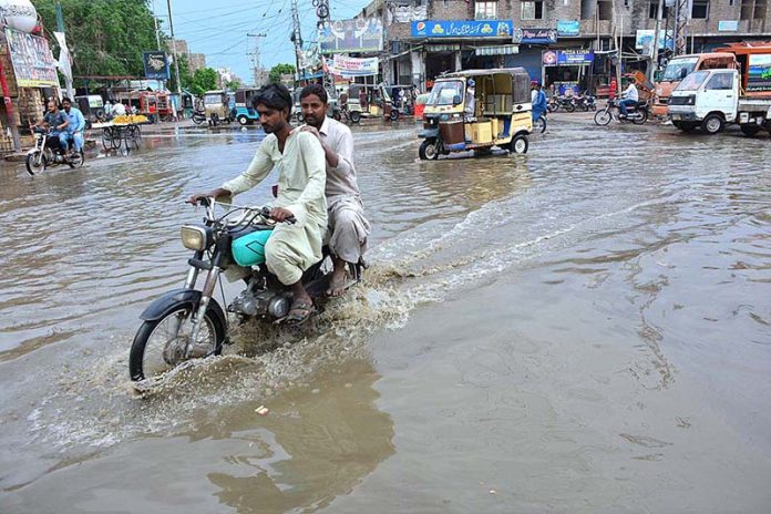 Vehicles passing through rain water accumulated on the road at Latifabad after the heavy rain in the city