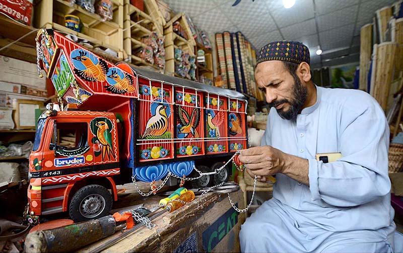 An artisan gives the final touch to a wooden made truck for decoration at his workplace