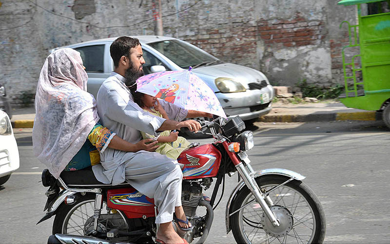 A motorcyclist with family using an umbrella to protect from heat in the city