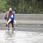 A woman carrying her daughter faces a challenging task of crossing stagnant water amidst heavy rainfall at IJP road
