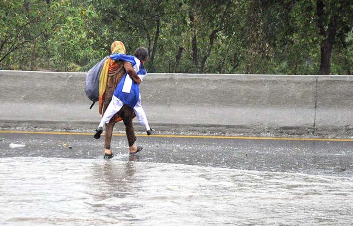 A woman carrying her daughter faces a challenging task of crossing stagnant water amidst heavy rainfall at IJP road